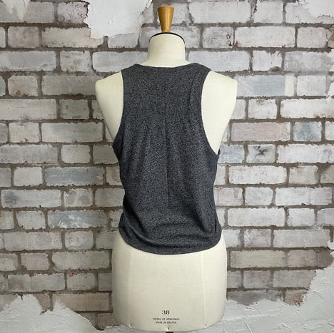 Mannequin wearing a gray tank top against a textured brick wall.