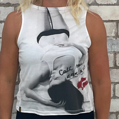 Woman wearing a sleeveless top with a graphic design in front of a textured brick wall.