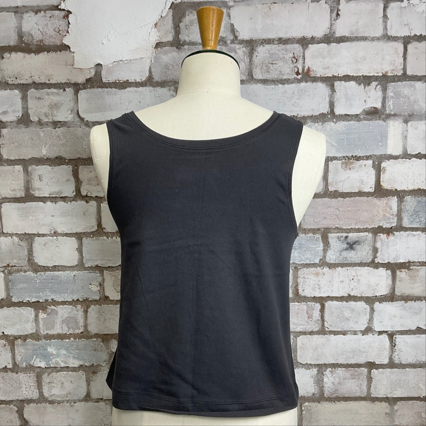 Black sleeveless top on a mannequin against a brick wall.