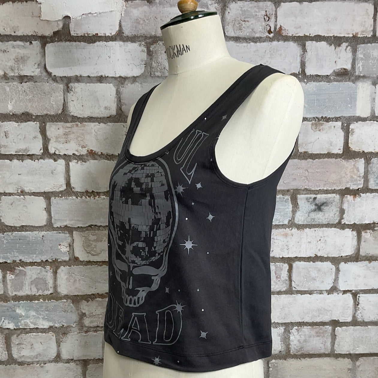 Black tank top with skull design on a mannequin against a brick wall.  Grateful Dead Tank top. Vest Top, Faded Grey Tank, sleeveless top