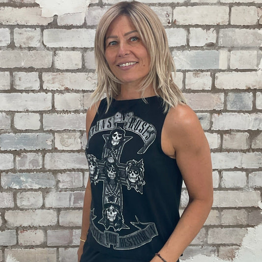 Woman wearing a black sleeveless Guns'N'Roses top with graphic design against a white brick wall.  Guns'N'Roses Appetite for Destruction slash neck tank top, vest top, upcycle by unwantees, anti landfill, Made in Great Britain