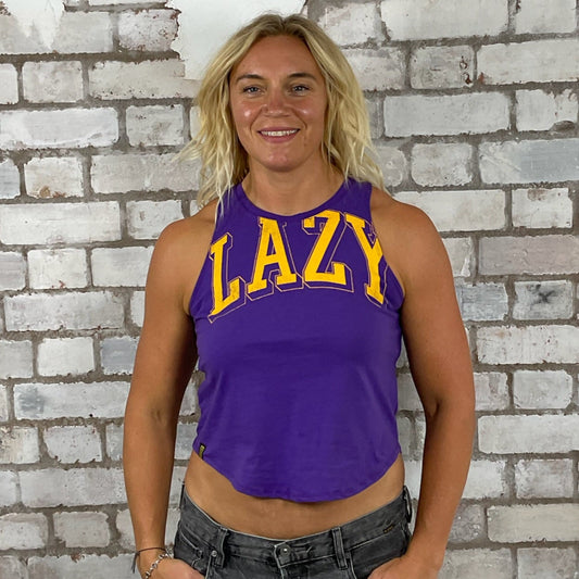 Person wearing a purple tank top with 'LAZY' text in front of a textured brick wall.  Lazy Yellow print on purple tank top, vest top, tshirt up cycle by Unwantees