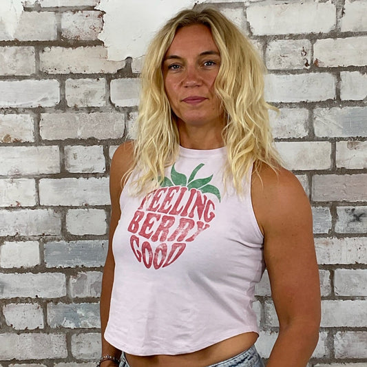 Woman wearing a tank top with feel good text and graphics against a textured white brick wall.  Pastel Shades Feeling Berry Good Unwantee, tank top, vest top, recycled fashion by Unwantees