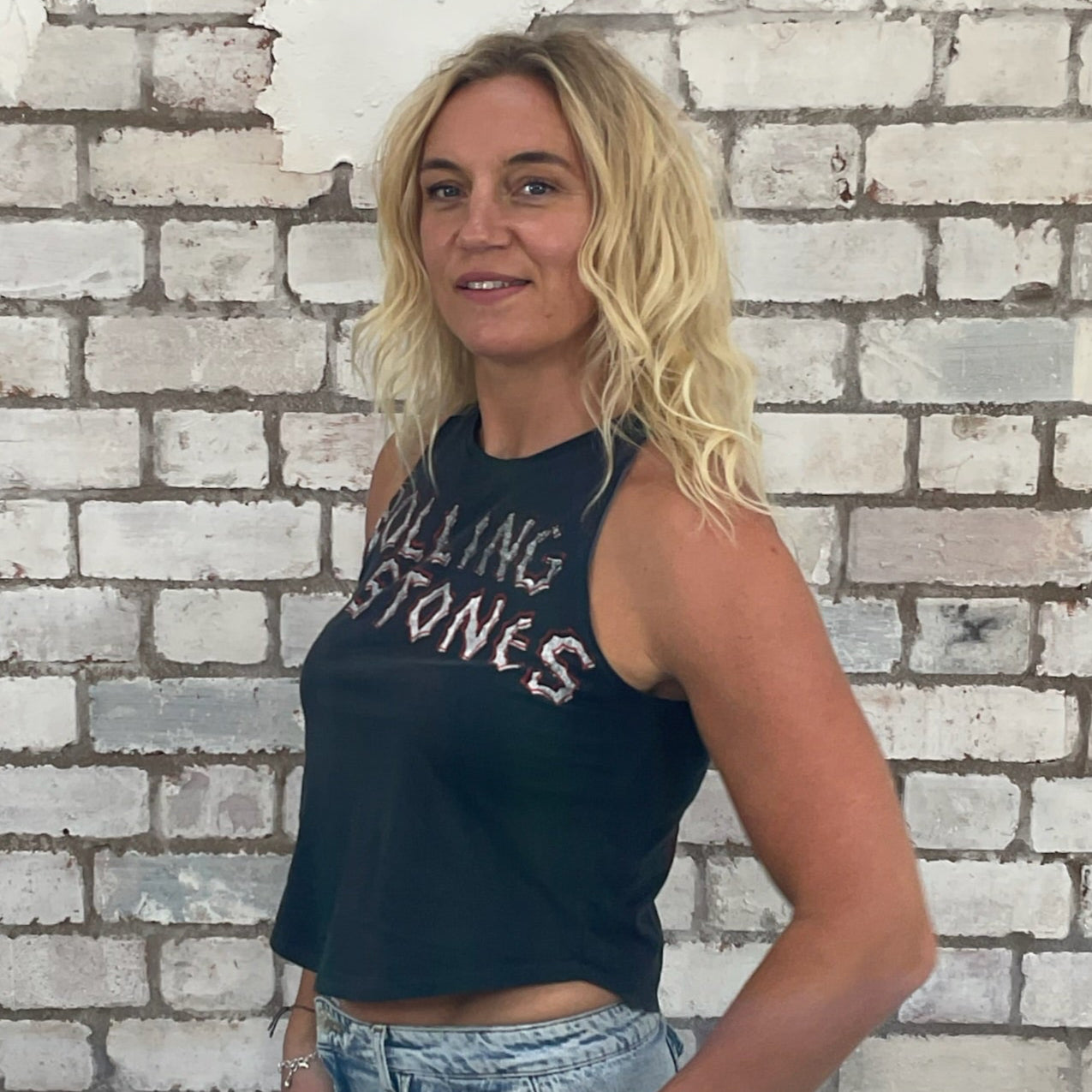 Woman wearing a Rolling Stones shirt against a textured white brick wall.  Rolling Stones Voodoo Lounge, Spikey tongue print,  front and back printed Tank Top by Unwantees, up cycled project by Unwantees, Recycled fashion by Unwantees.co.uk, racerback style