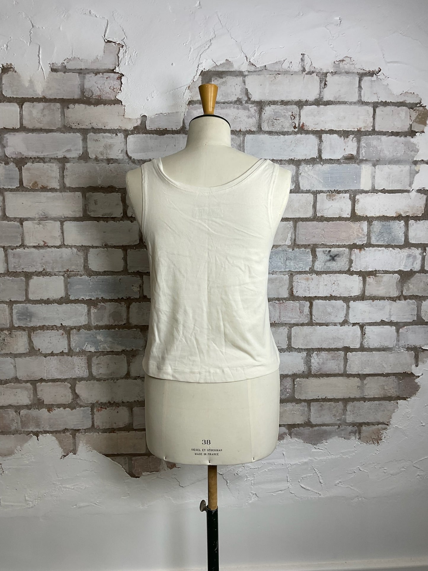 White sleeveless top on a mannequin against a textured brick wall.