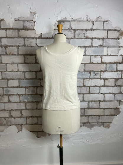 White sleeveless top on a mannequin against a textured brick wall.