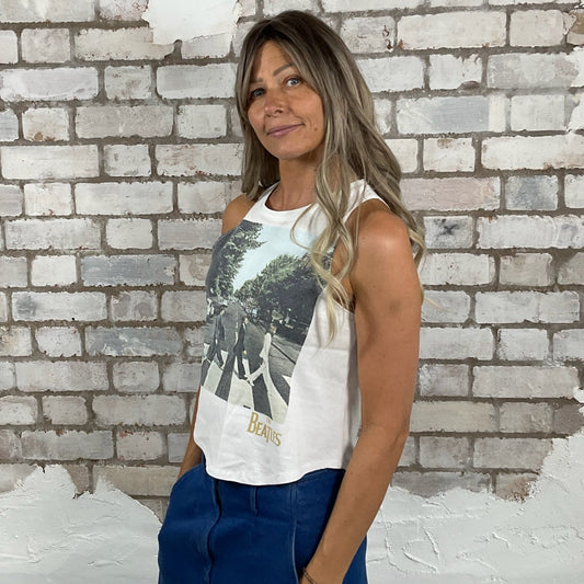 Woman wearing a sleeveless graphic top and blue pants standing against a textured brick wall. The Beatles Merch, Abbey Road, Racerback, tank top, vest top, Unwantees upcycle, recycled fashion, up cycled tshirt