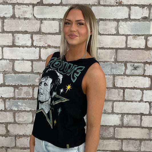 Woman wearing a black sleeveless Bowie shirt with graphic design against a brick wall.  one-of-a-kind clothing
unique tank tops / unique vests
handmade clothing UK
reworked t-shirts UK
limited edition fashion
sustainable streetwear
sustainable tank tops
women’s eco fashion UK
