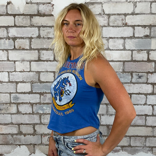 Woman wearing a blue tank top with a graphic design against a textured white brick wall.  sustainable fashion UK
eco-friendly clothing UK
upcycled t-shirts / upcycled tank tops
ethical fashion brand UK
zero waste clothing
slow fashion brand
made in Britain clothing
sustainable vest tops