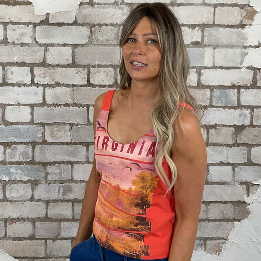 Woman wearing a colorful tank top with a Virginia State scenic design against a textured brick wall. Virginia Graphic print tank top, Virginia State Vest, Up Cycled fashion by Unwantees