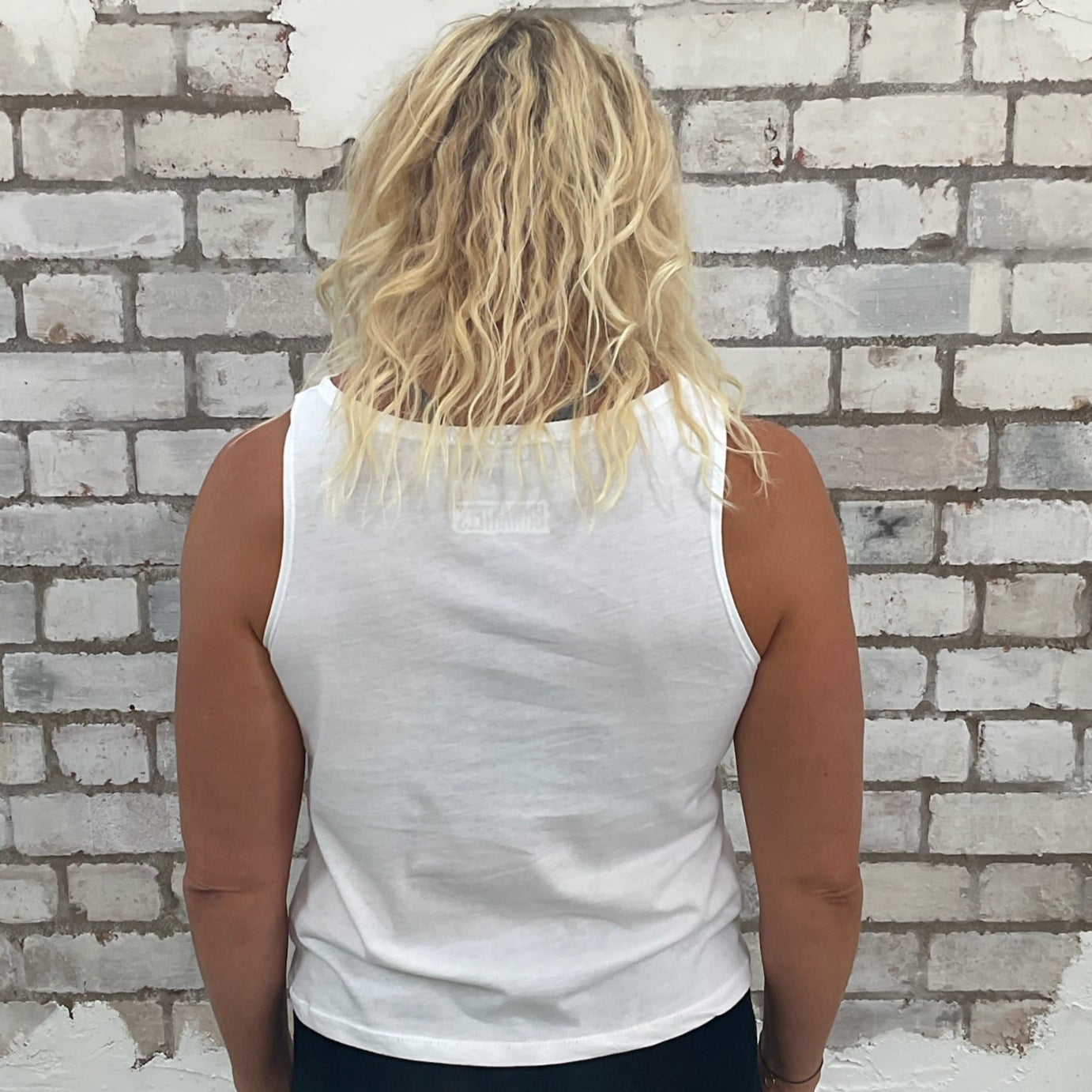 Person wearing a white sleeveless top against a textured brick wall.