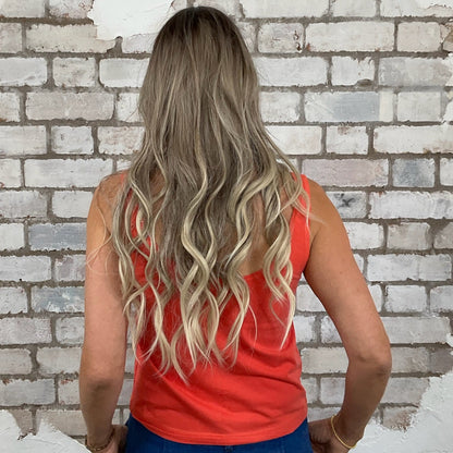 Woman with long blonde hair wearing a red top and blue jeans standing in front of a white brick wall.  Woman wearing a colorful tank top with a scenic nature design against a white brick wall.  Unwantees Virginia Graphic print tank top, Virginia State Vest, Up Cycled fashion by Unwantees