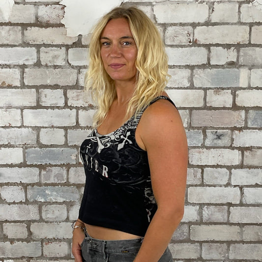 Woman standing in front of a textured white brick wall Xzavier clothing unwantee, tank top, vest top, scoop neck tank top, heavy metal print 