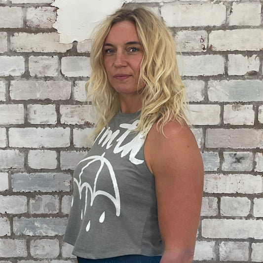 Woman wearing a gray tank top with a white graphic design against a brick wall.  bmth Unwantees, Recycled clothing, sustainable fashion, athleisure wear, band tees, upcycled graphic tshirts, fashion recycled, Sustainable Fashion