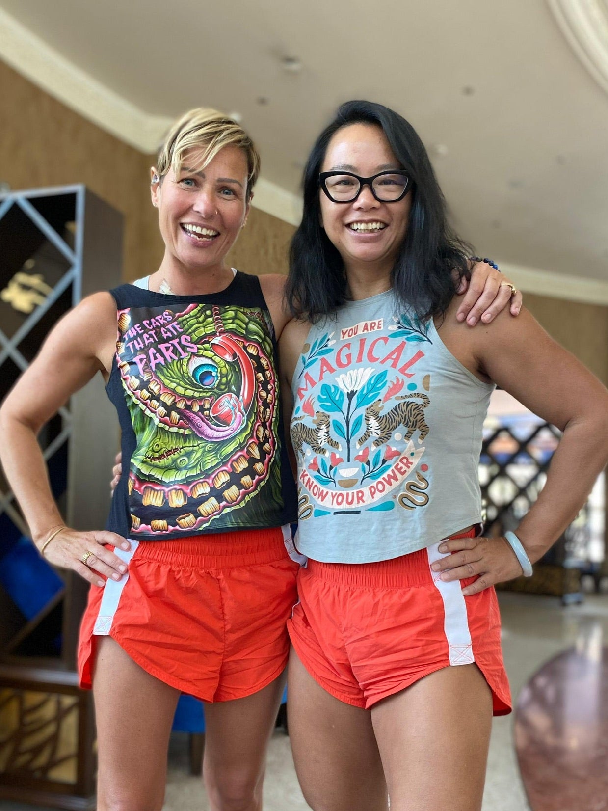 Two middle-aged women with arms around each other, both wearing graphic Unwantee tank tops, upcycled sustainable clothing