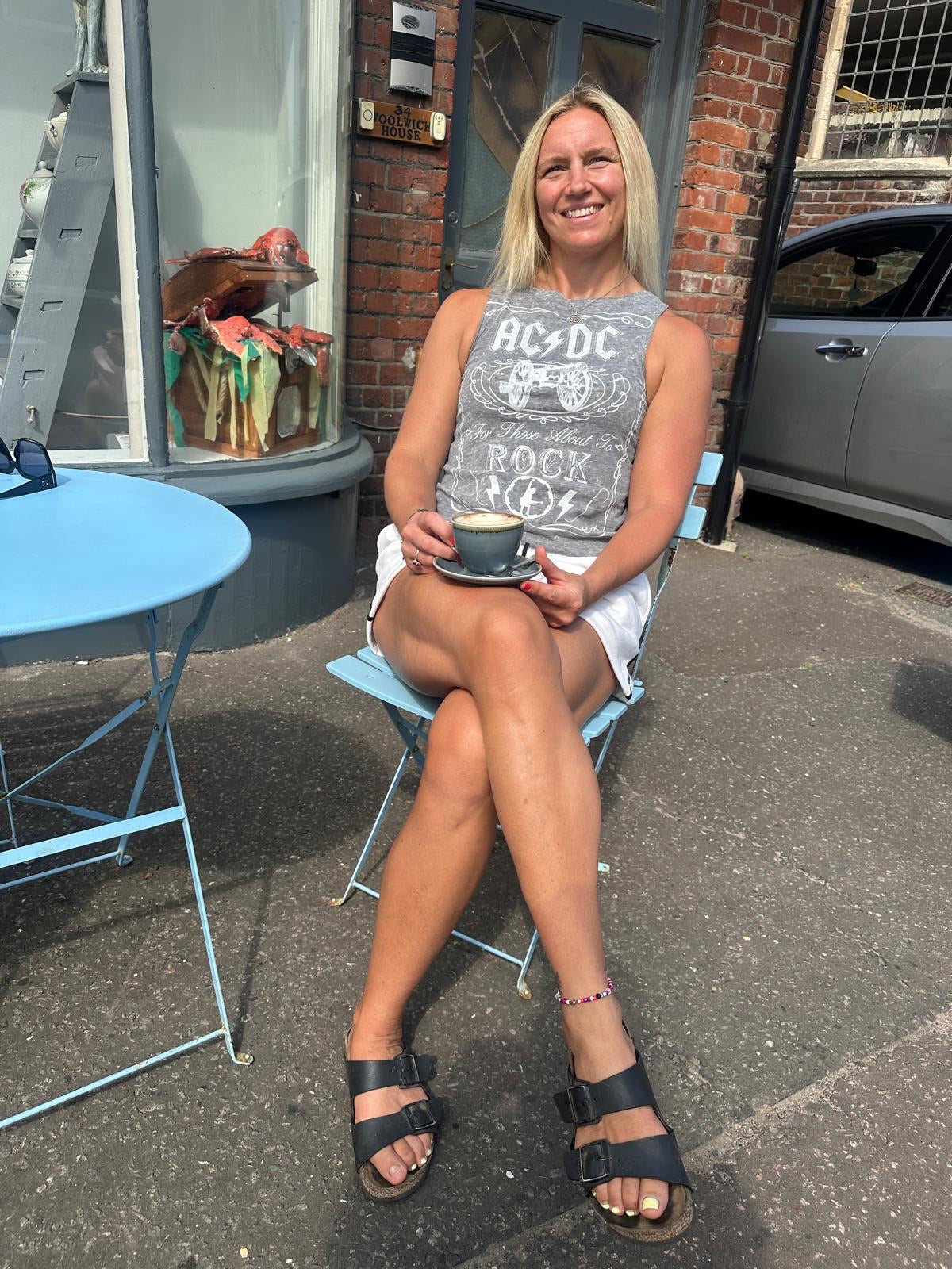 Woman smiling while sitting with a coffee, wearing a grey AC/DC graphic Unwantee tank top