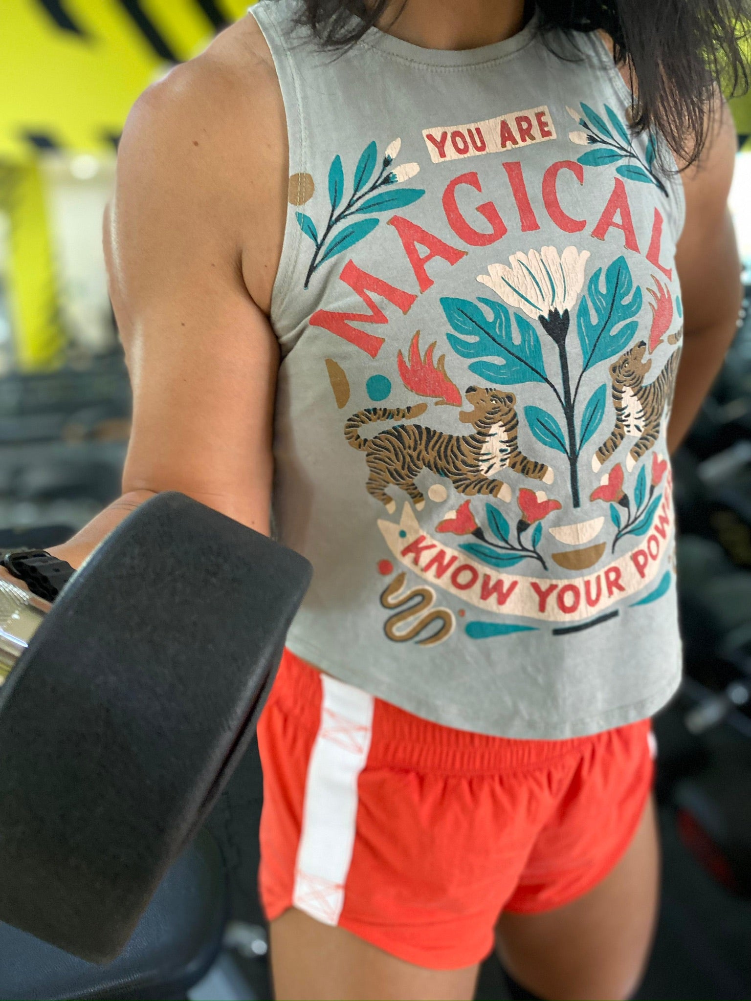 Woman wearing a graphic Unwantee tank top while working out in the gym