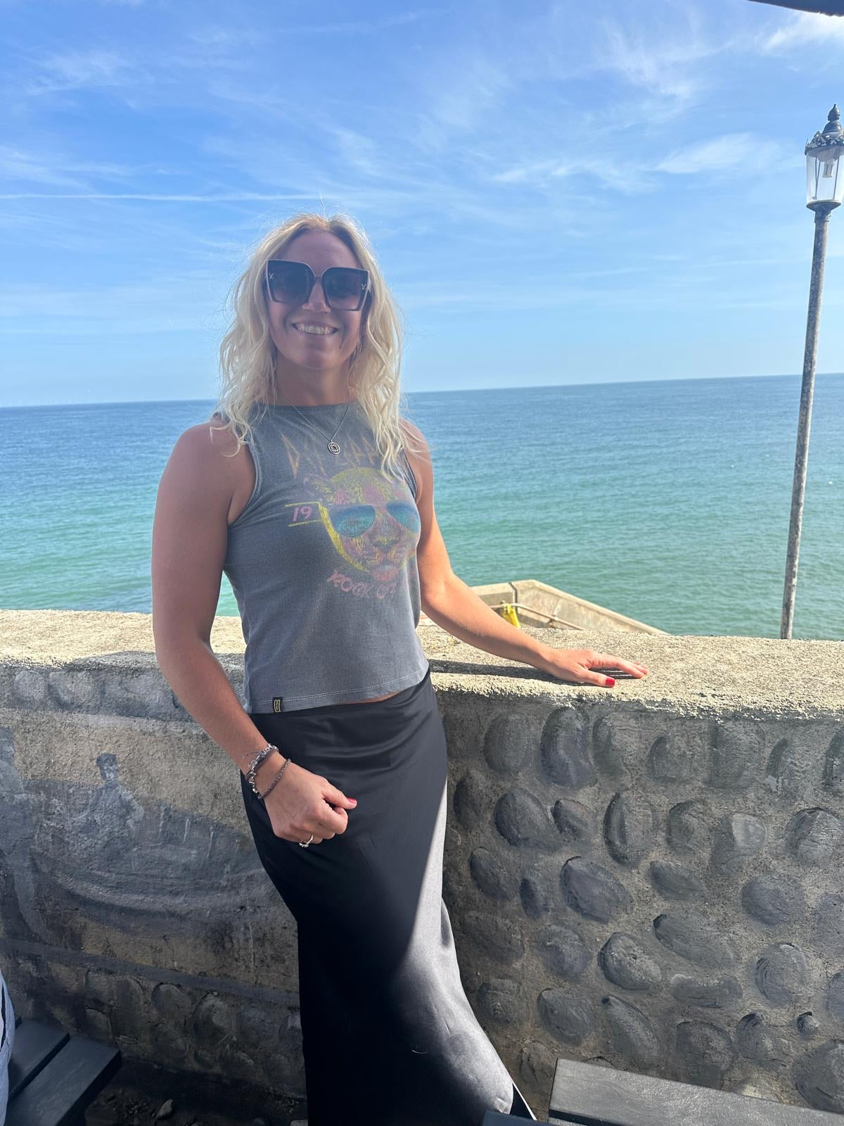 Woman wearing a graphic Unwantee tank top with a sea view in the background