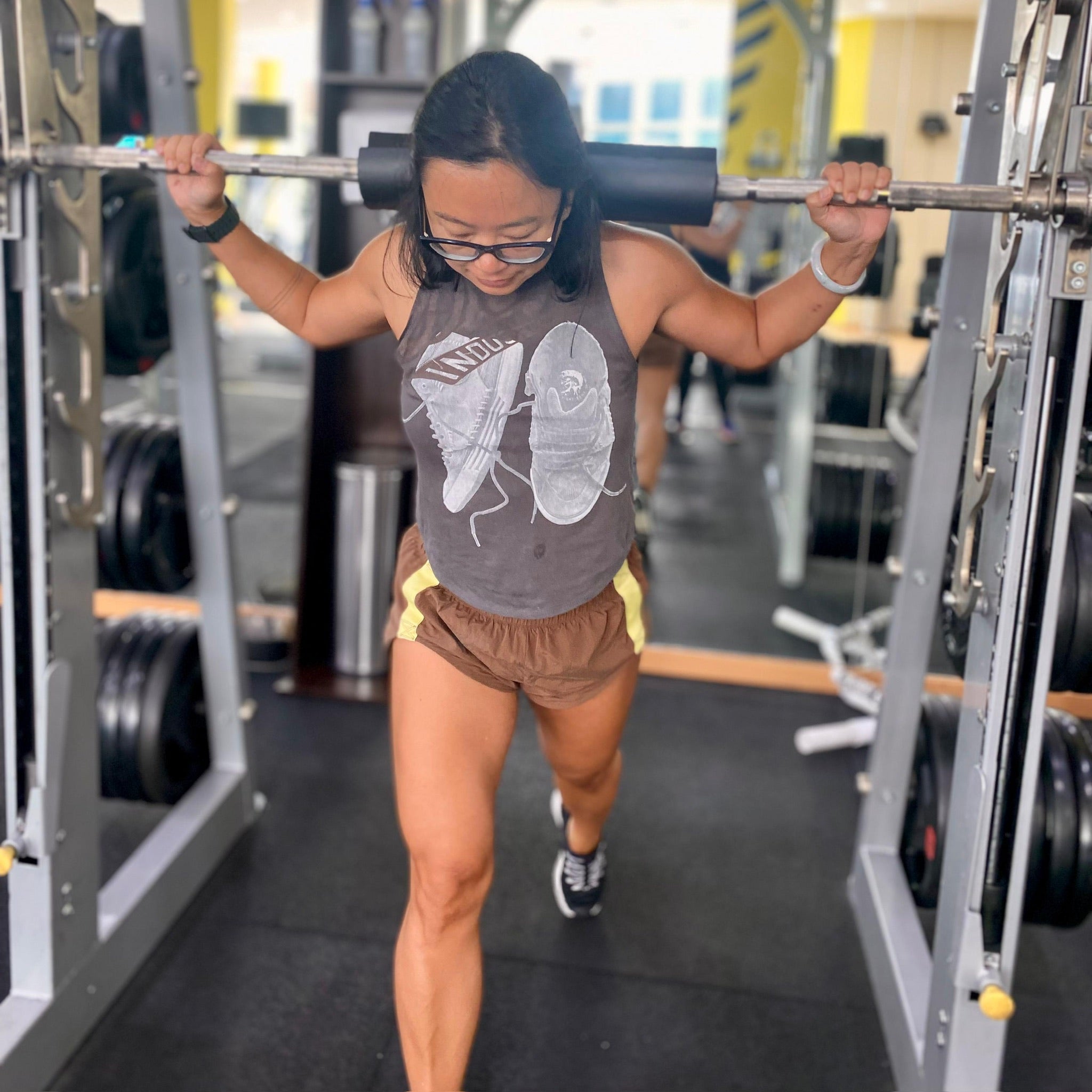 Woman doing back lunges on a Smith machine in the gym wearing a graphic Unwantee t-shirt with trainer illustrations